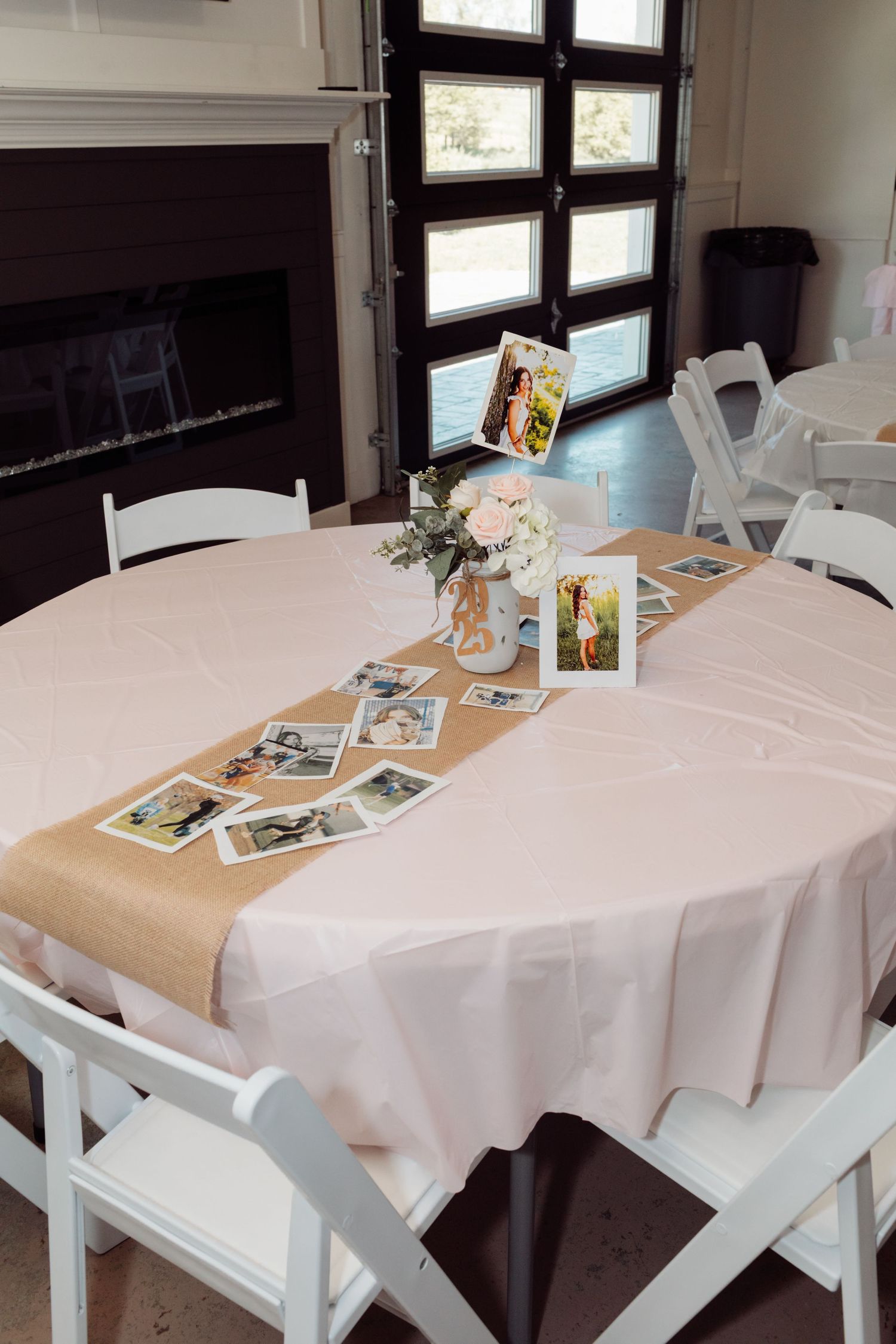 Elegant oval table with burlap runner, pink tablecloth, floral centerpiece, and scattered photos for a party.