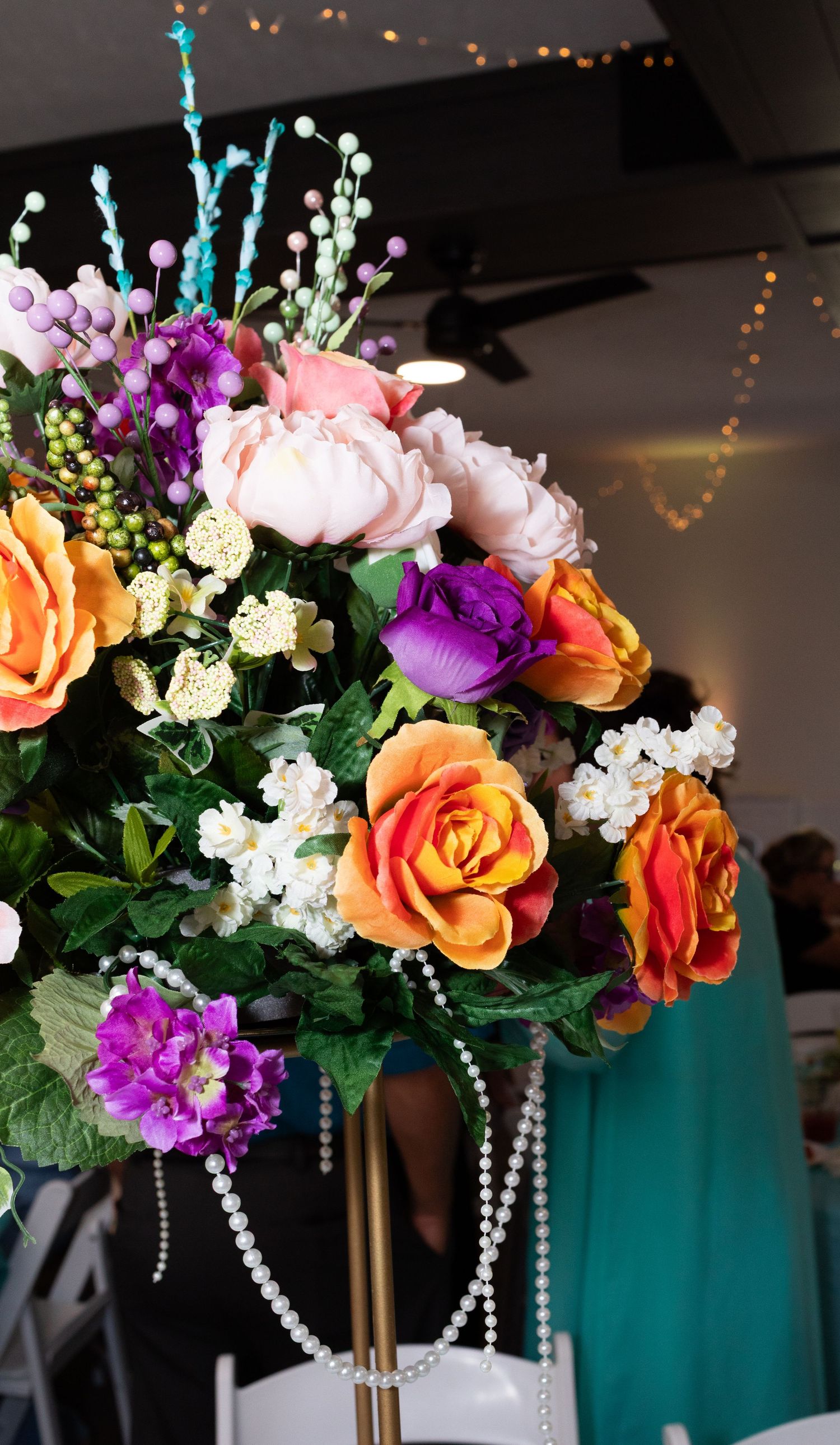 Colorful wedding centerpiece with orange, purple, and pink artificial flowers adorned with pearl strands.