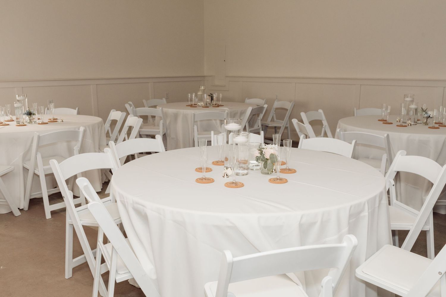 Elegant wedding reception hall with round tables, white linens, and white folding chairs.