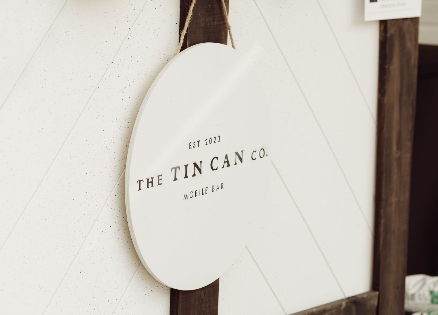 Oval white sign for The Tin Can Co. Mobile Bar, established 2022, hanging on a white shiplap wall.