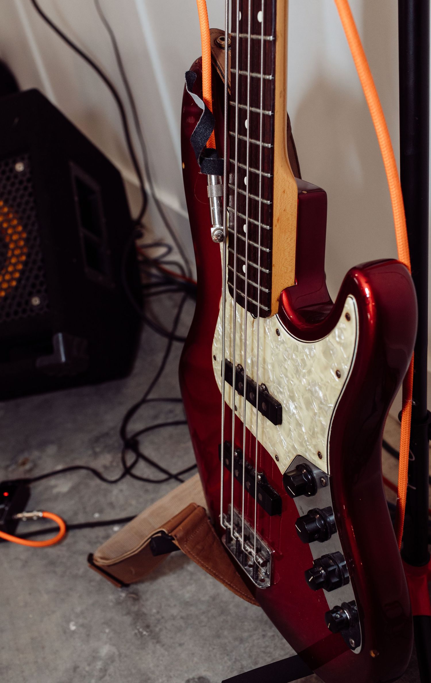 Red metallic bass guitar on a wooden stand with orange cables and amp.