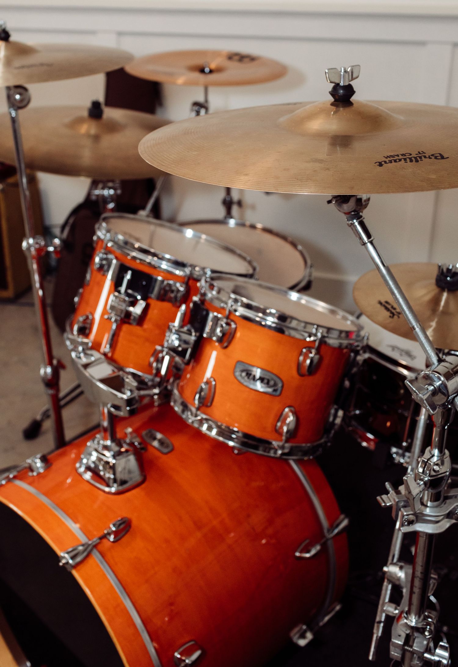 Orange burst drum kit with cymbals on stands in a bright room.