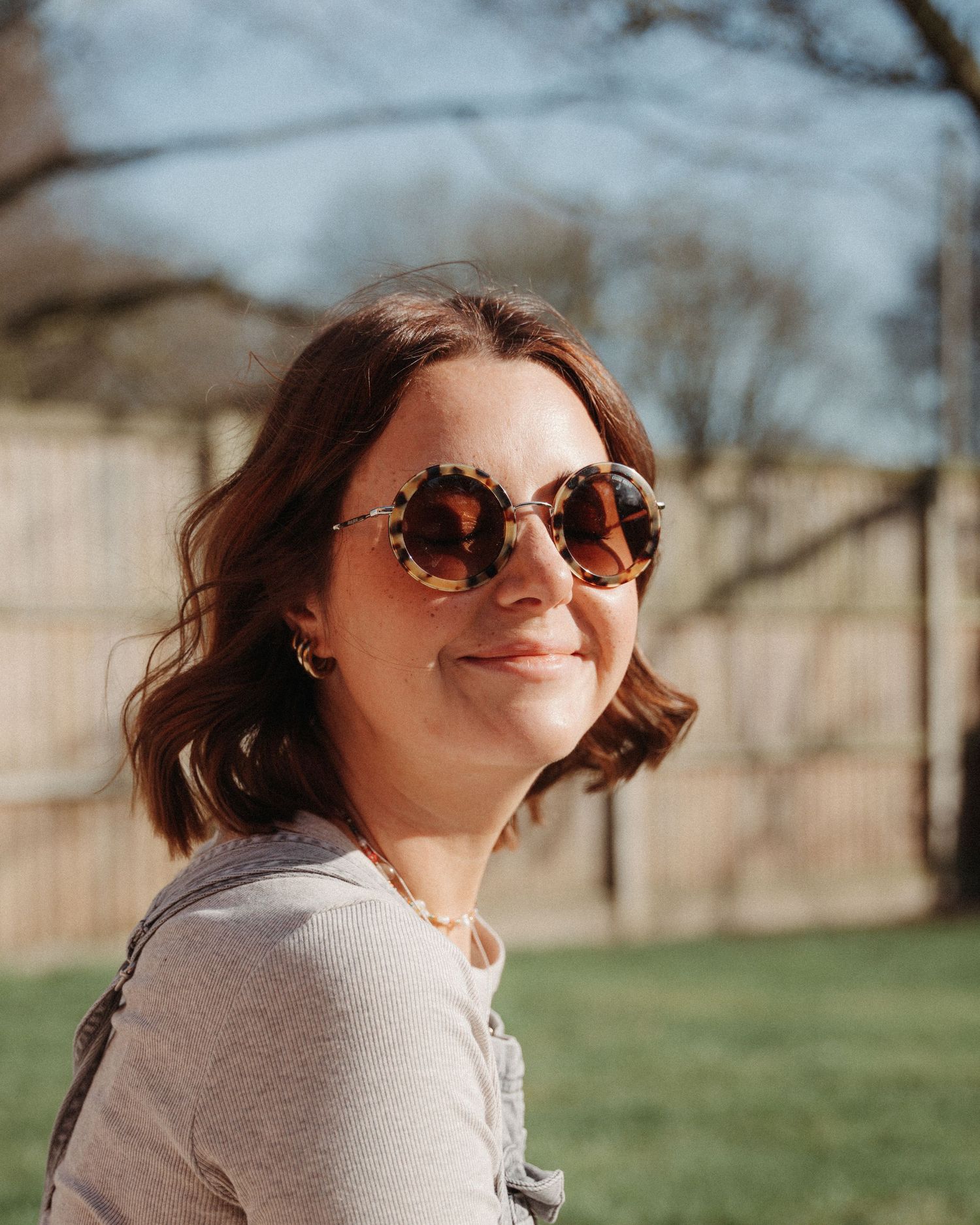 Woman in sunglasses smiling outdoors on sunny day.