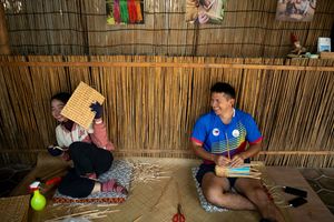 Tourists sitting on bamboo mats inside a traditional shelter with woven walls.