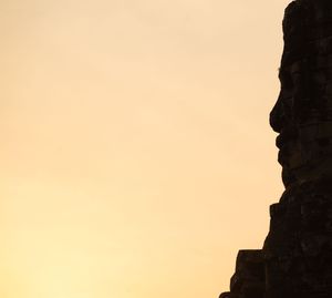 Silhouetted temple ruins against an orange sunset sky at Angkor Wat.