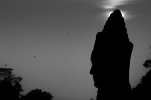 Ancient stone statue silhouetted against a misty sky with birds flying in the background.