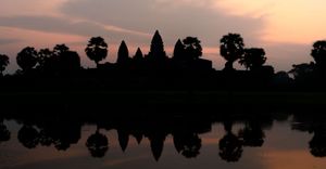 Silhouette of Angkor Wat temple complex reflected in still water during sunset.