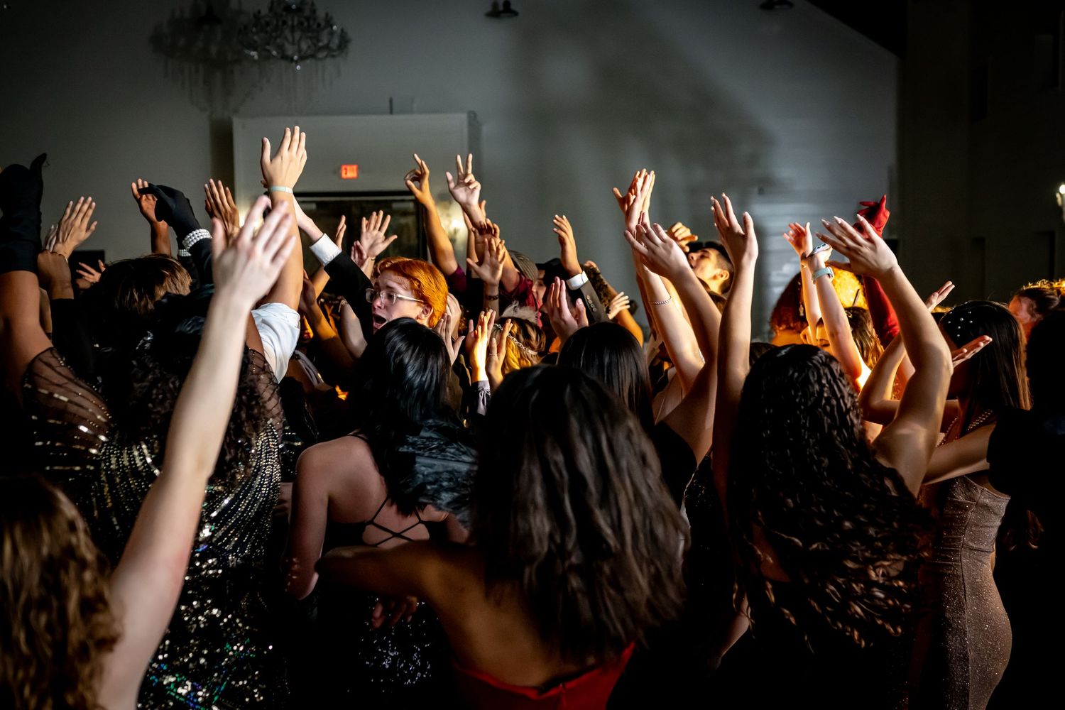 Energetic crowd raises hands in the air at a dark music concert venue with dramatic lighting.