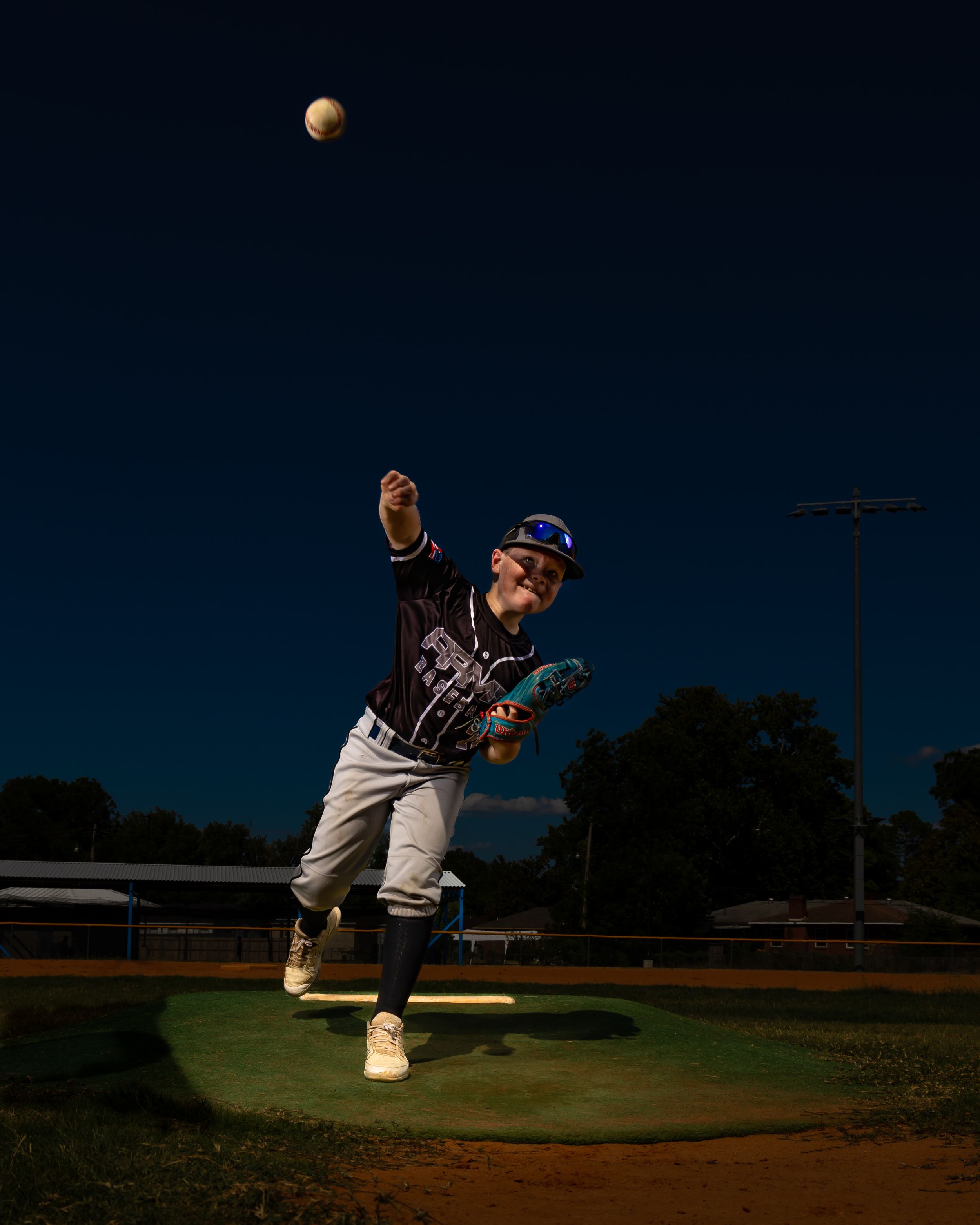 Baseball player leaps to catch a ball against a dramatic dark sky with the moon visible in the background.