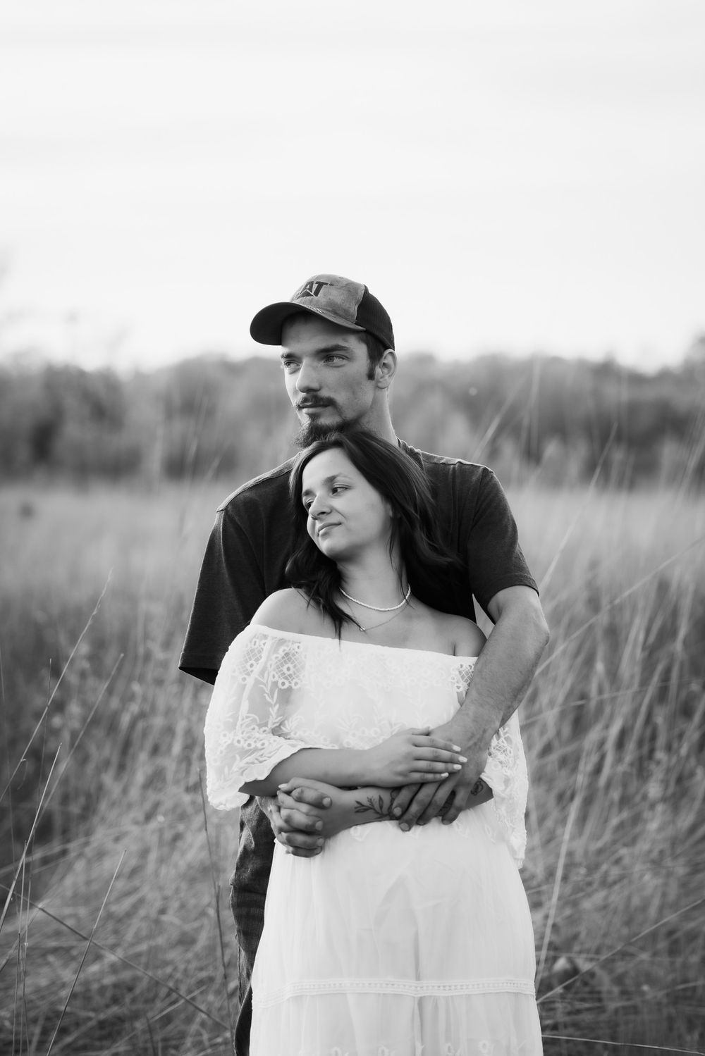 Black and white portrait of couple embracing in tall grass.