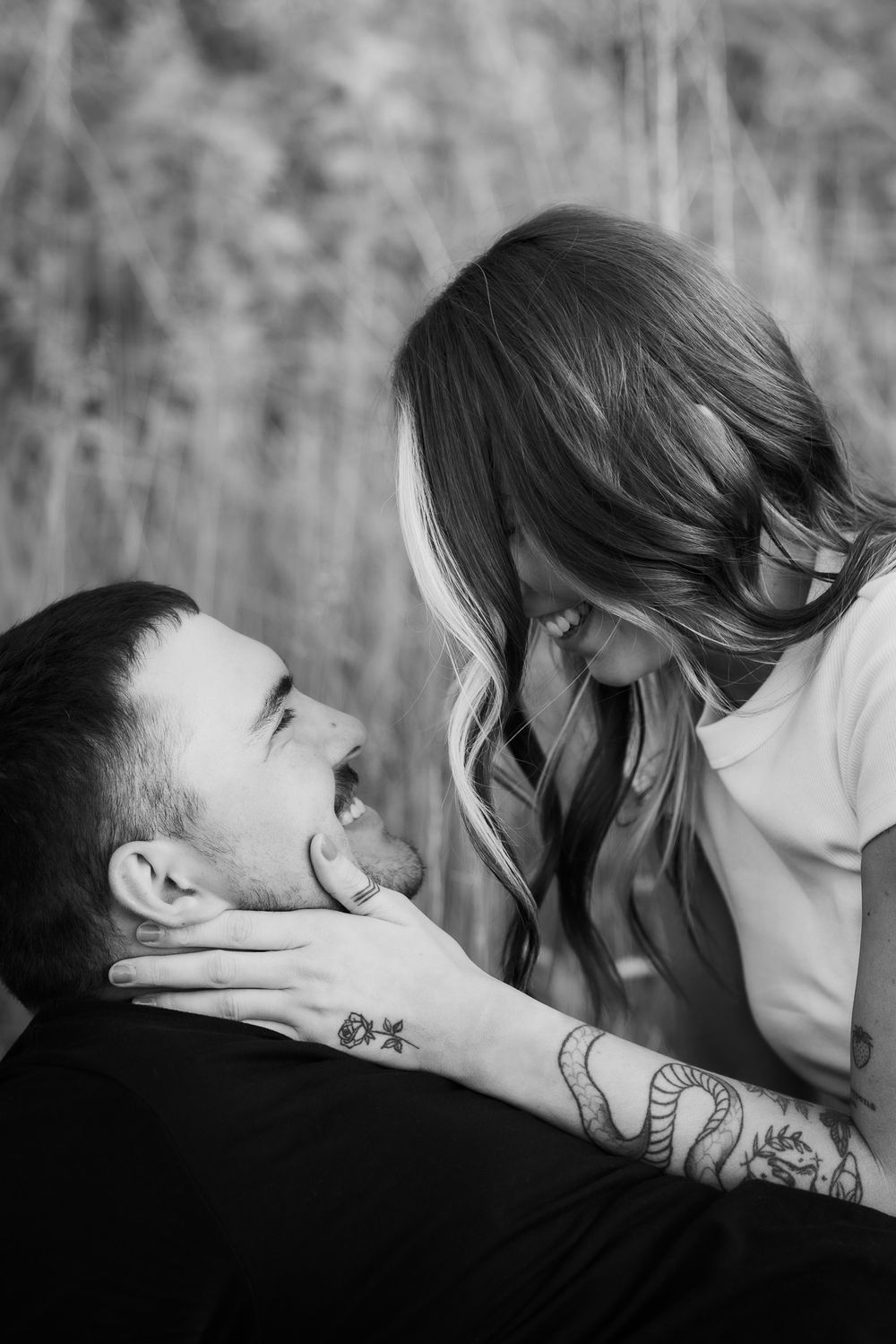 Black and white close-up of couple sharing playful moment with tattooed hand.