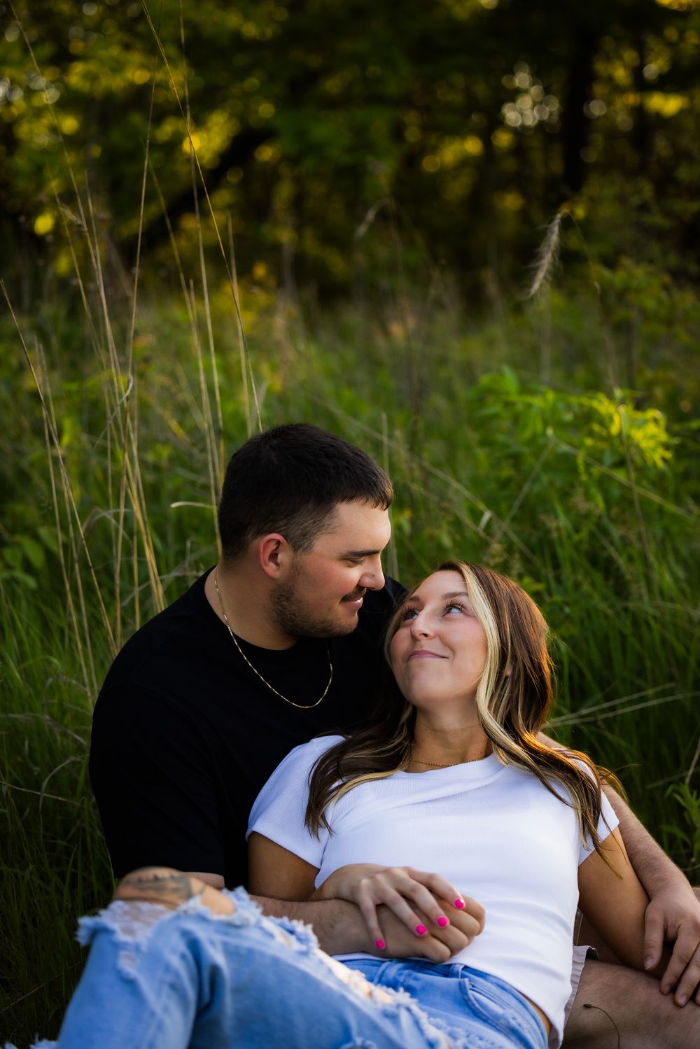 Couple relaxing together in tall grass during golden hour nature photoshoot.