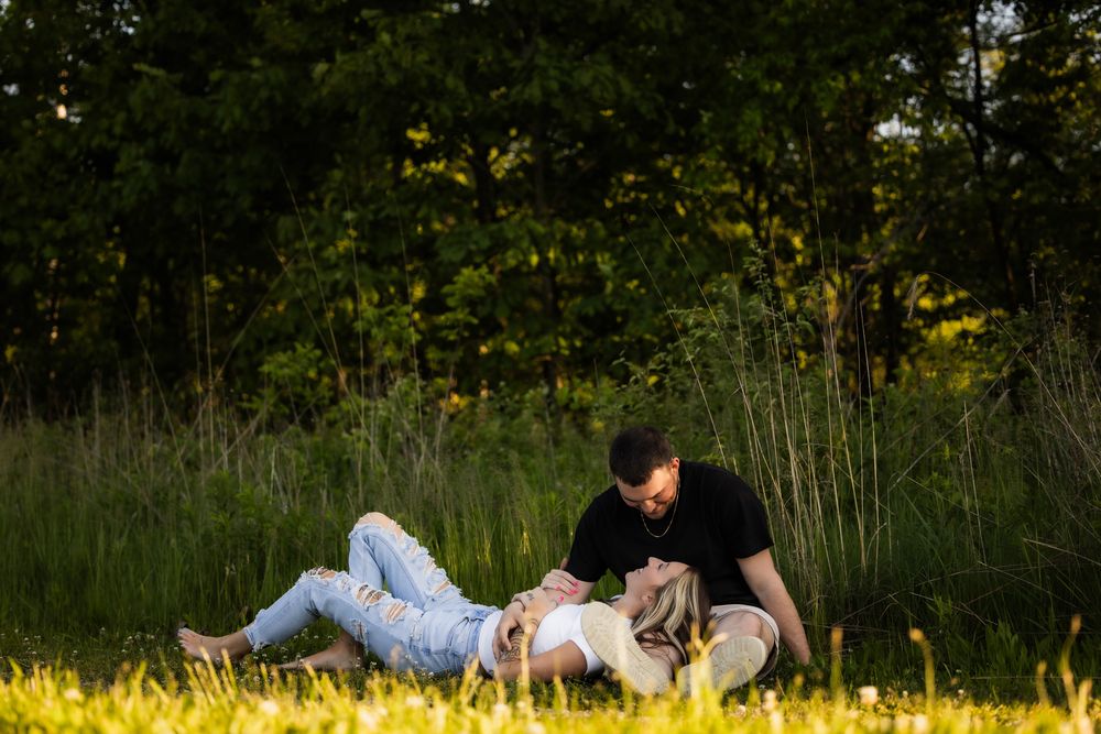 Couple laying in sunny meadow surrounded by tall grass and wildflowers.
