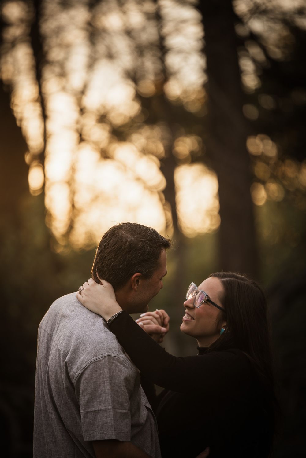 A romantic couple shares an intimate moment at sunset with golden bokeh lights filtering through trees in the background.