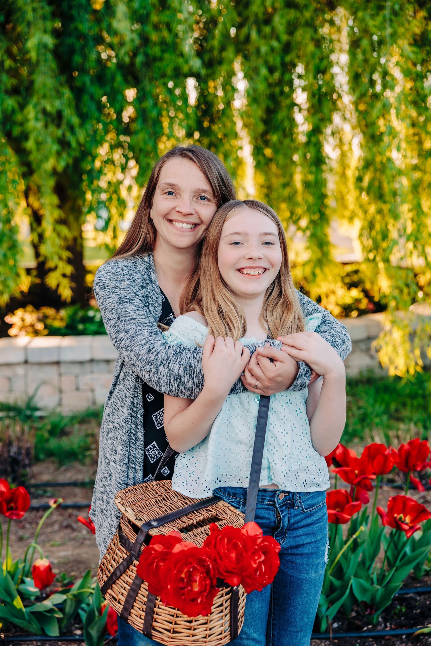 Two friends embracing in a garden with red tulips and willow trees on a sunny spring day.