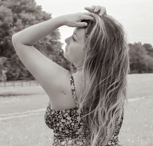 Young woman with long blonde hair in a floral dress poses in a field on a sunny day.