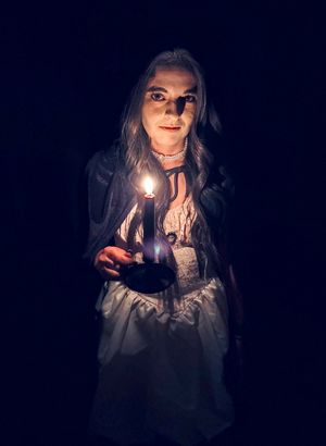 Dramatic candlelit portrait in vintage dress against dark background.