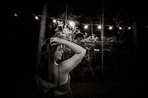 A silhouetted figure poses under string lights at night in an outdoor setting.