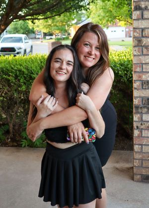 Two friends in black outfits embracing and smiling outdoors.