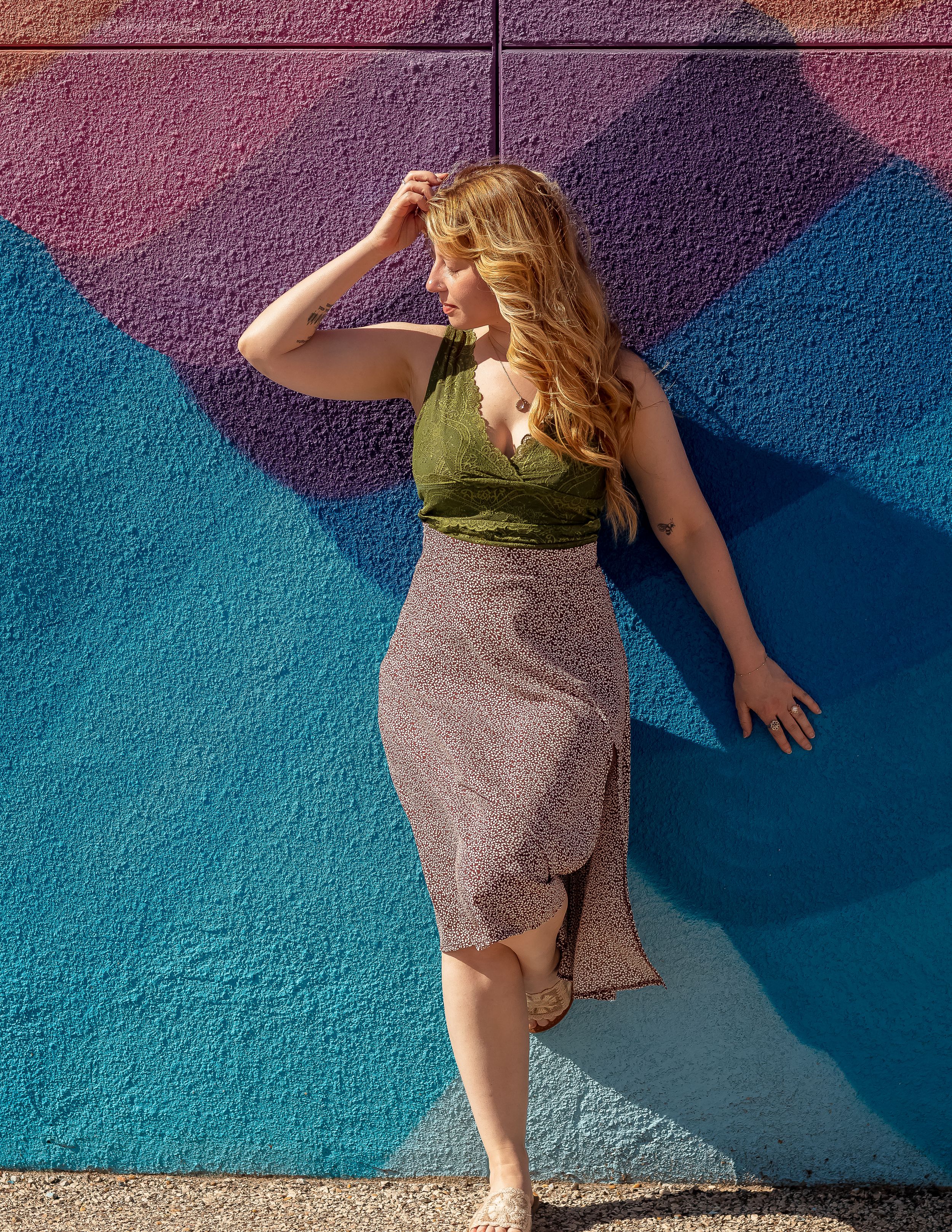 A person in a green top and gray skirt poses dramatically against a vibrant blue and purple wall.