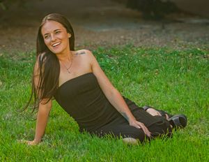 Person in a black strapless dress reclines on green grass during an outdoor photo session.