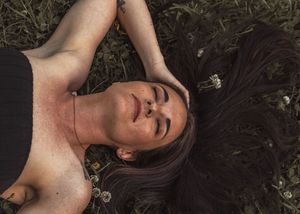 Person with dark hair lying in grass with small white flowers scattered around.