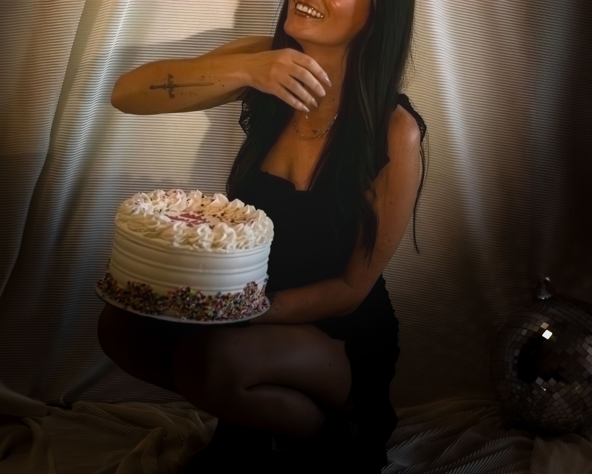 A beautifully decorated white frosted cake with pink rosettes sits on display in a moody, dimly lit setting.