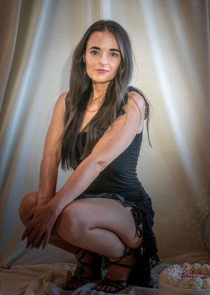Elegant portrait in a black dress with long dark hair against a light background and textured curtains.