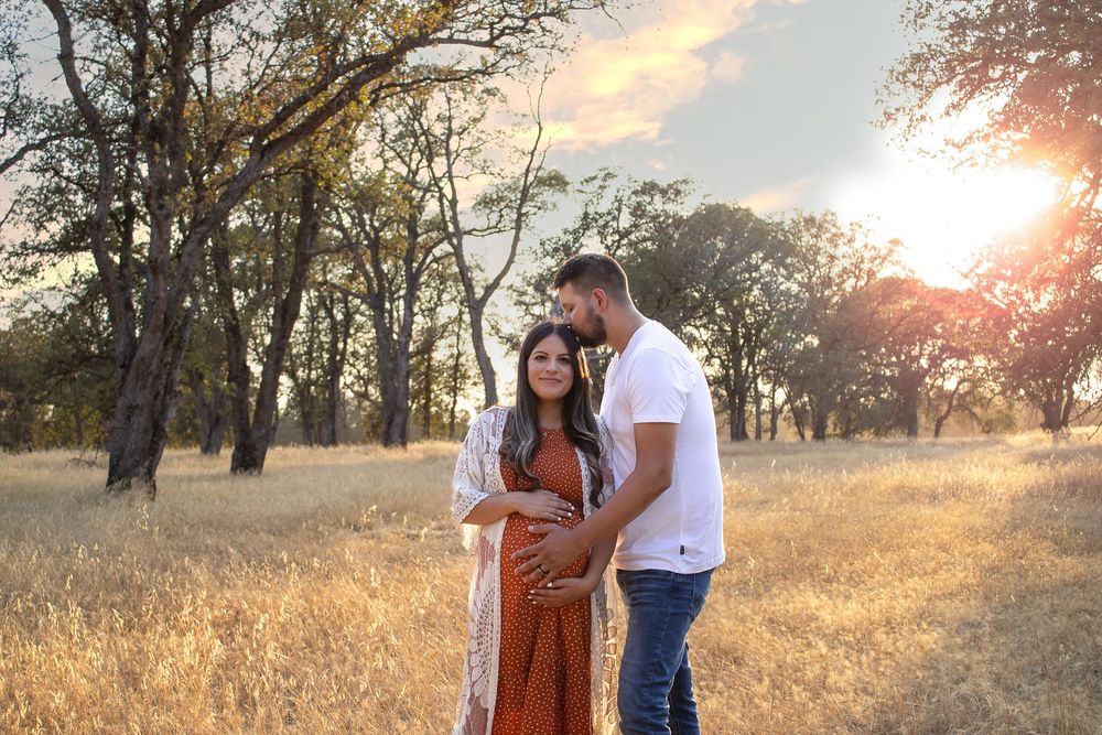 A maternity photoshoot in a golden field at sunset with the couple in casual attire.