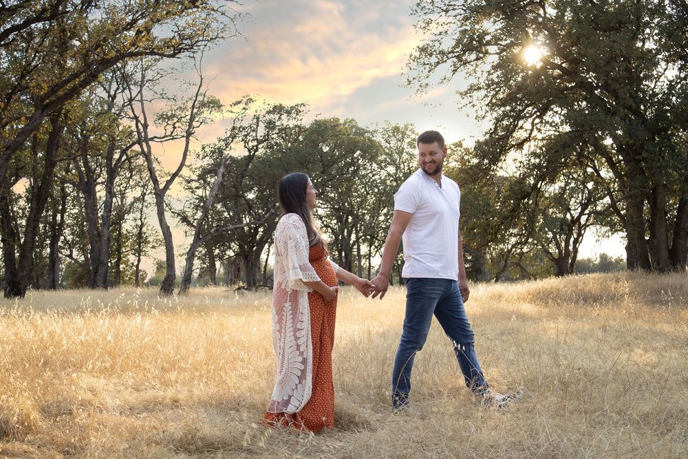 A couple walking through a sun-drenched field during golden hour surrounded by oak trees.