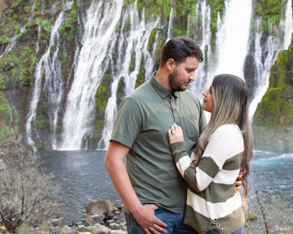 A tender moment shared between a couple in front of a majestic waterfall.