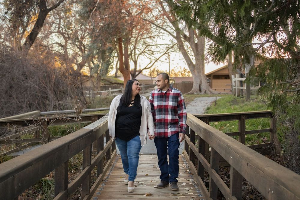 A couple walking hand in hand across a wooden bridge surrounded by trees at sunset.