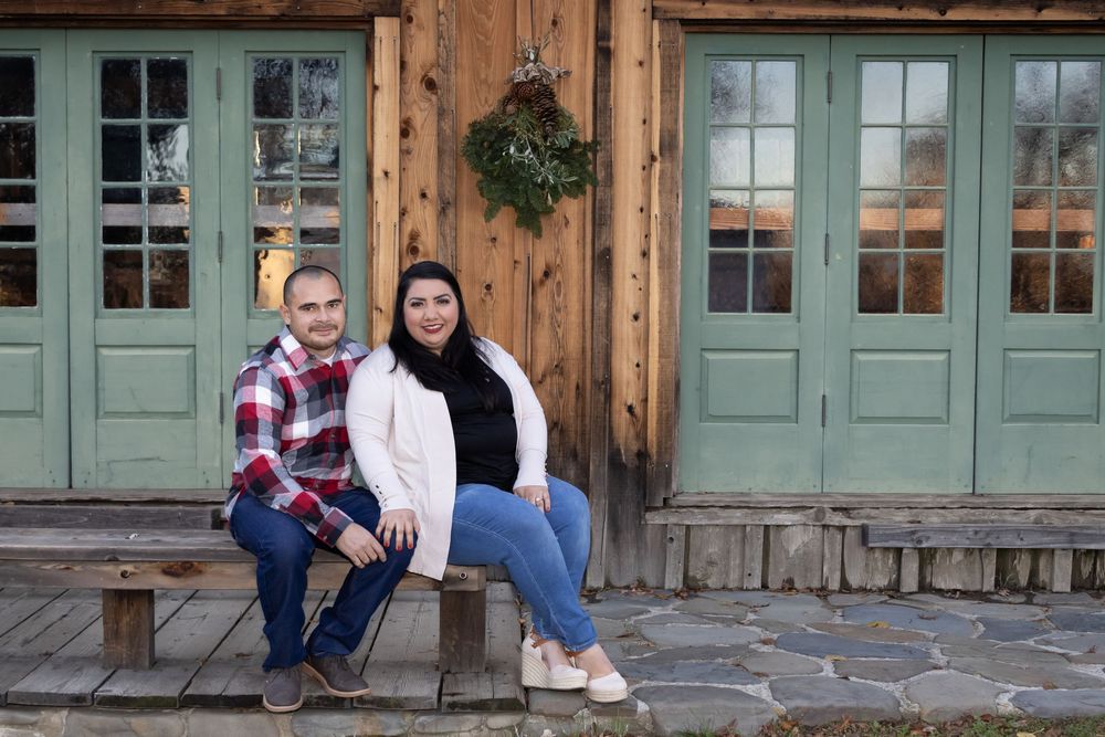 A couple sitting on a rustic wooden porch with mint green doors and natural wood siding.