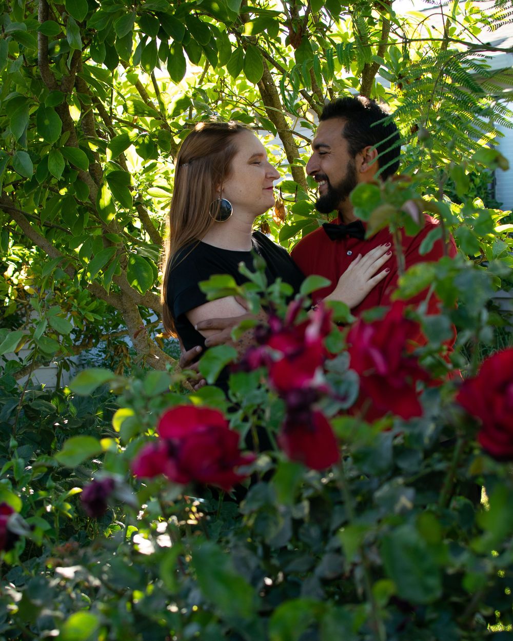 A romantic portrait of a couple surrounded by roses and green leaves in a garden setting.