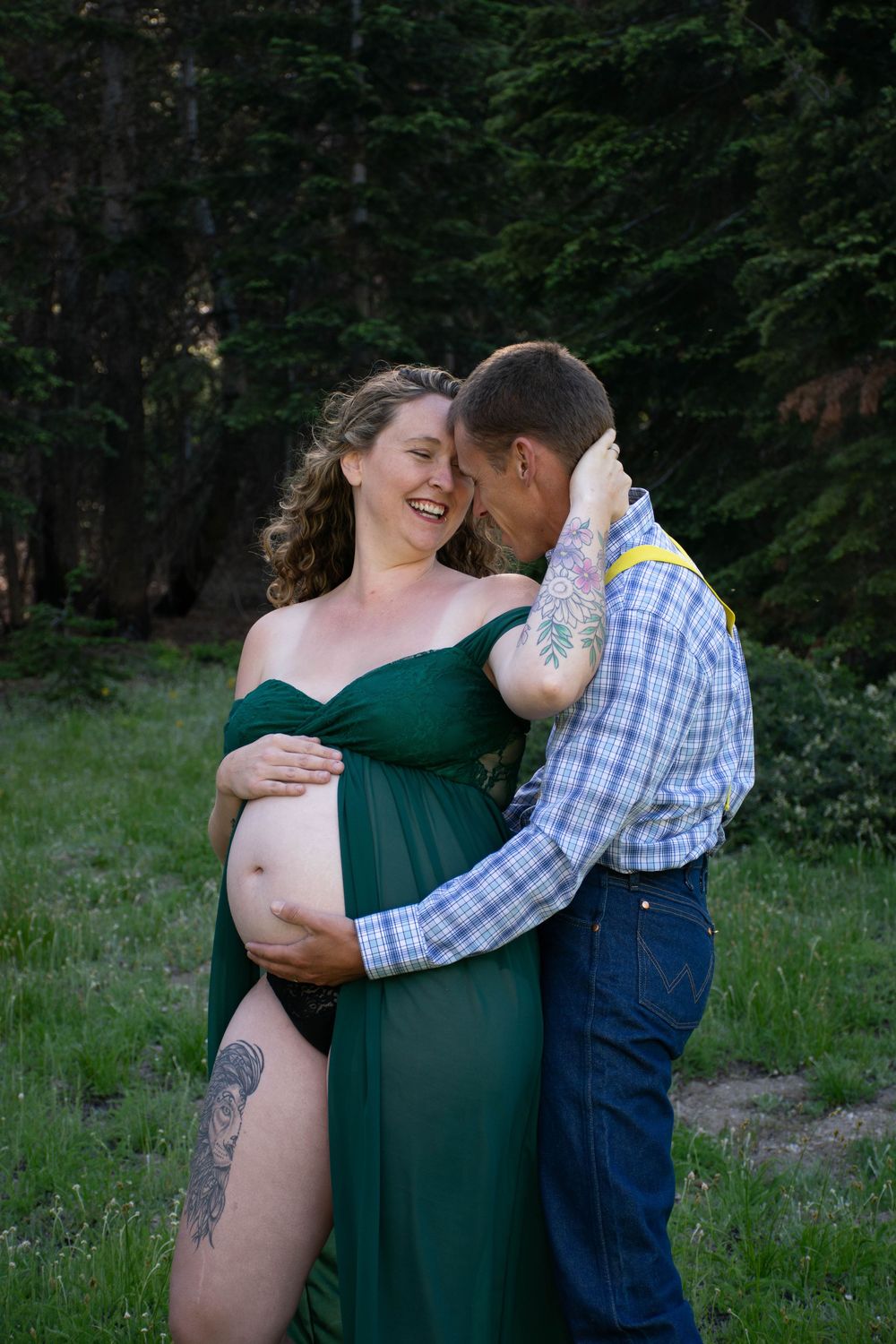 A maternity photoshoot in the forest with a couple embracing, the pregnant woman wearing an emerald green dress.