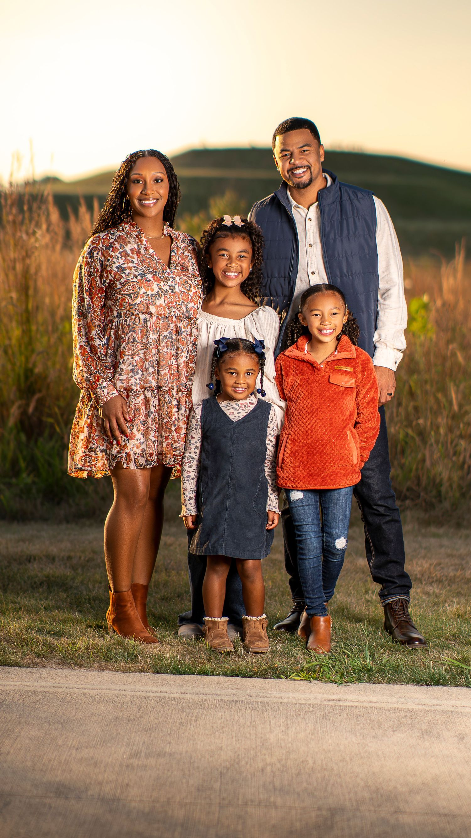 Outdoor portrait of a family group standing together at sunset in a grassy field.
