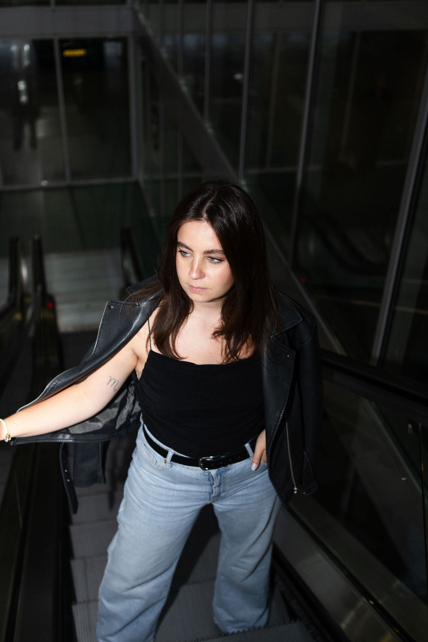 Atmospheric portrait on escalator showing casual style with black top and light denim.