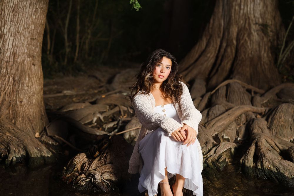 Artistic portrait of someone in white dress near large tree roots.