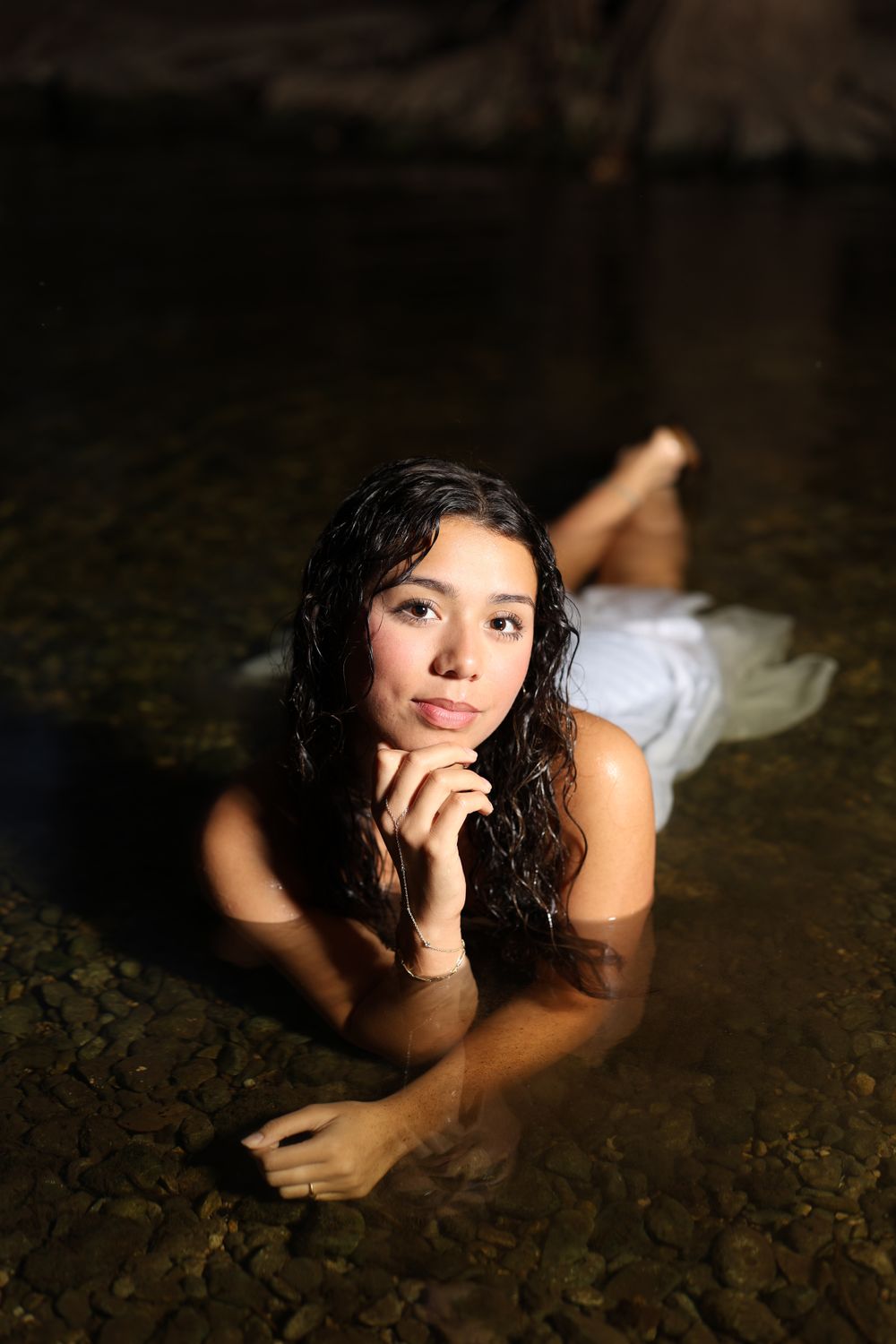 Artistic portrait lying on rocky shore in dramatic lighting.