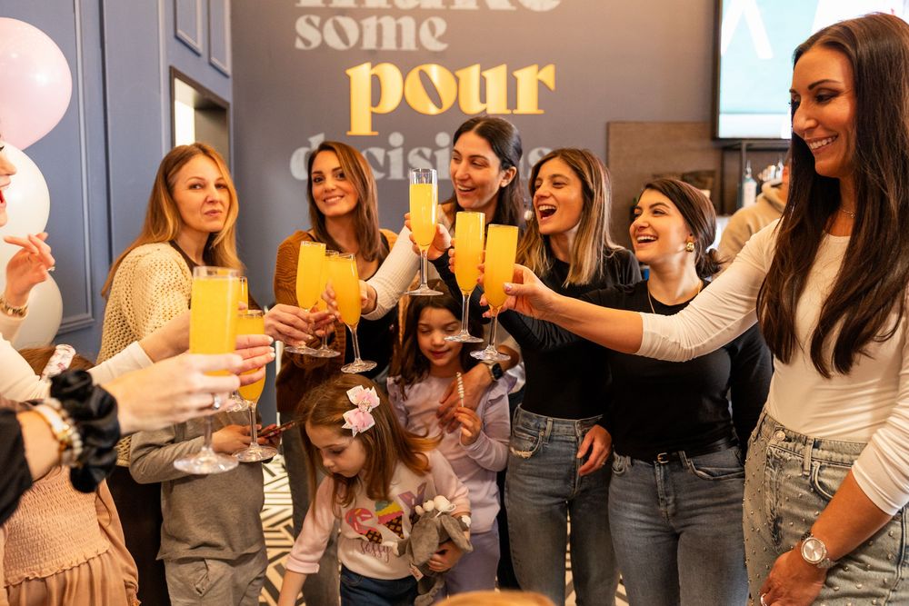 A group of friends toasting with yellow cocktails at a casual gathering with a decorative wall quote in the background.