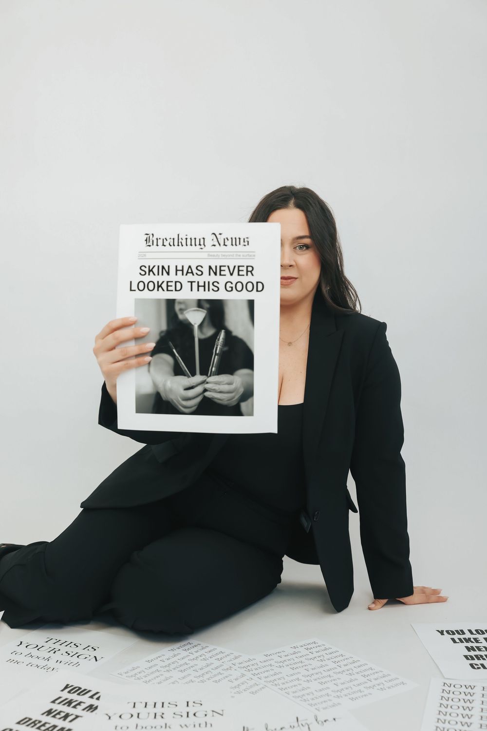 Woman in black suit sitting on floor holding Breaking News magazine reading Skin Has Never Looked This Good.