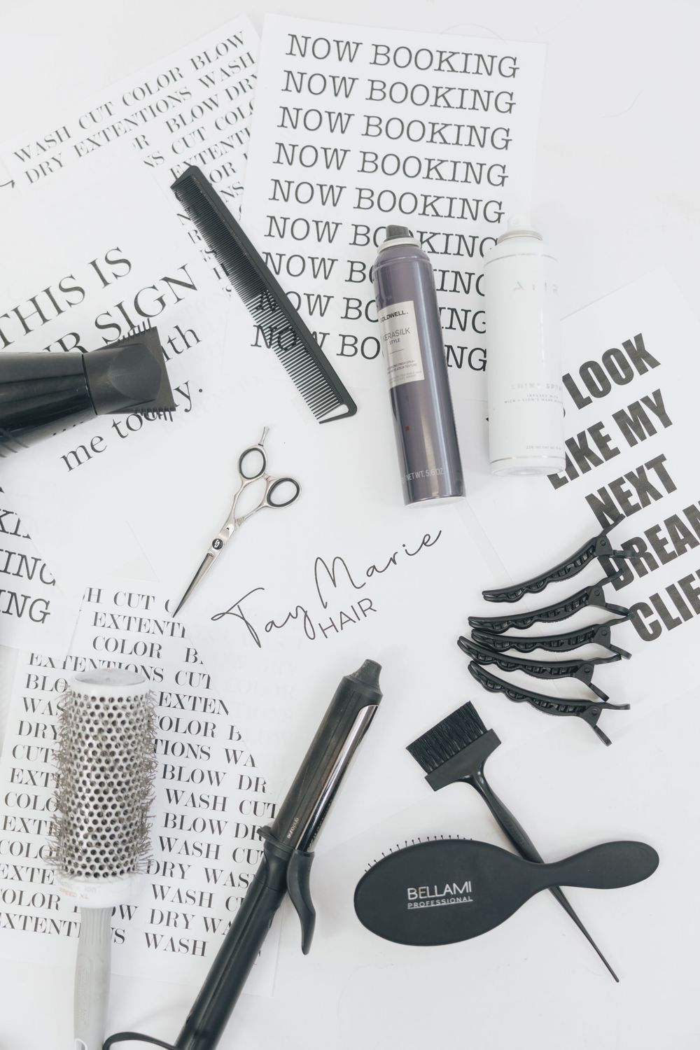 Flat lay of hair styling tools including scissors, flat iron, comb, and clips with Tay Marie Hair branding cards.