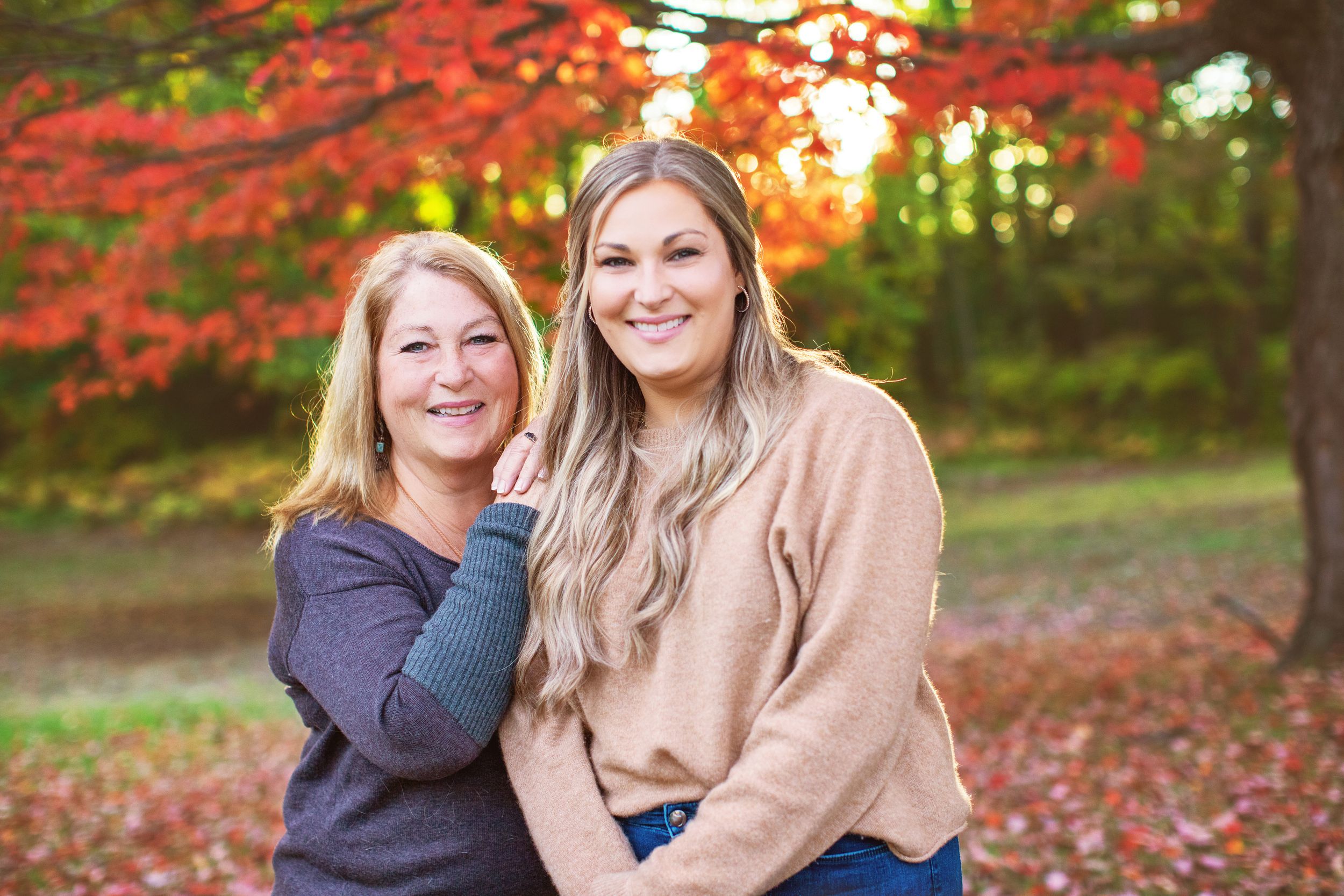 Two people sitting together outdoors in autumn with vibrant red maple leaves in the background.