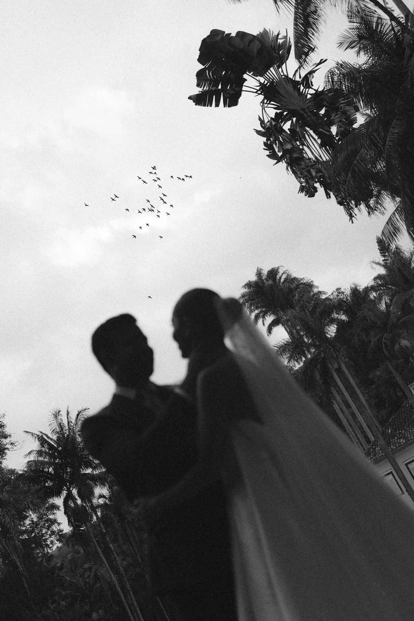 Black and white portrait of a bride tossing her bouquet while wearing a flowing wedding dress.