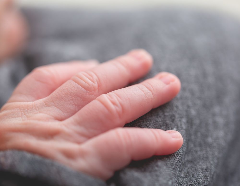 Close-up of a newborn baby's delicate hand with tiny fingers resting on a soft gray blanket.