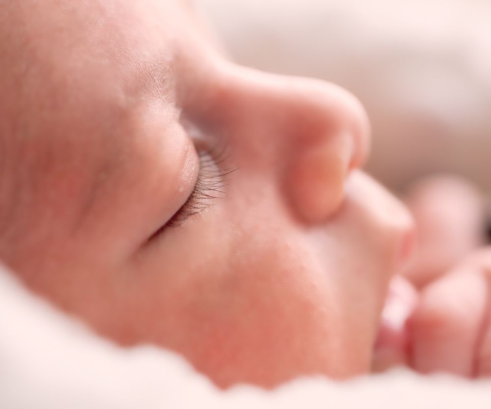 Close-up of a sleeping newborn baby with delicate eyelashes resting peacefully on a white surface.