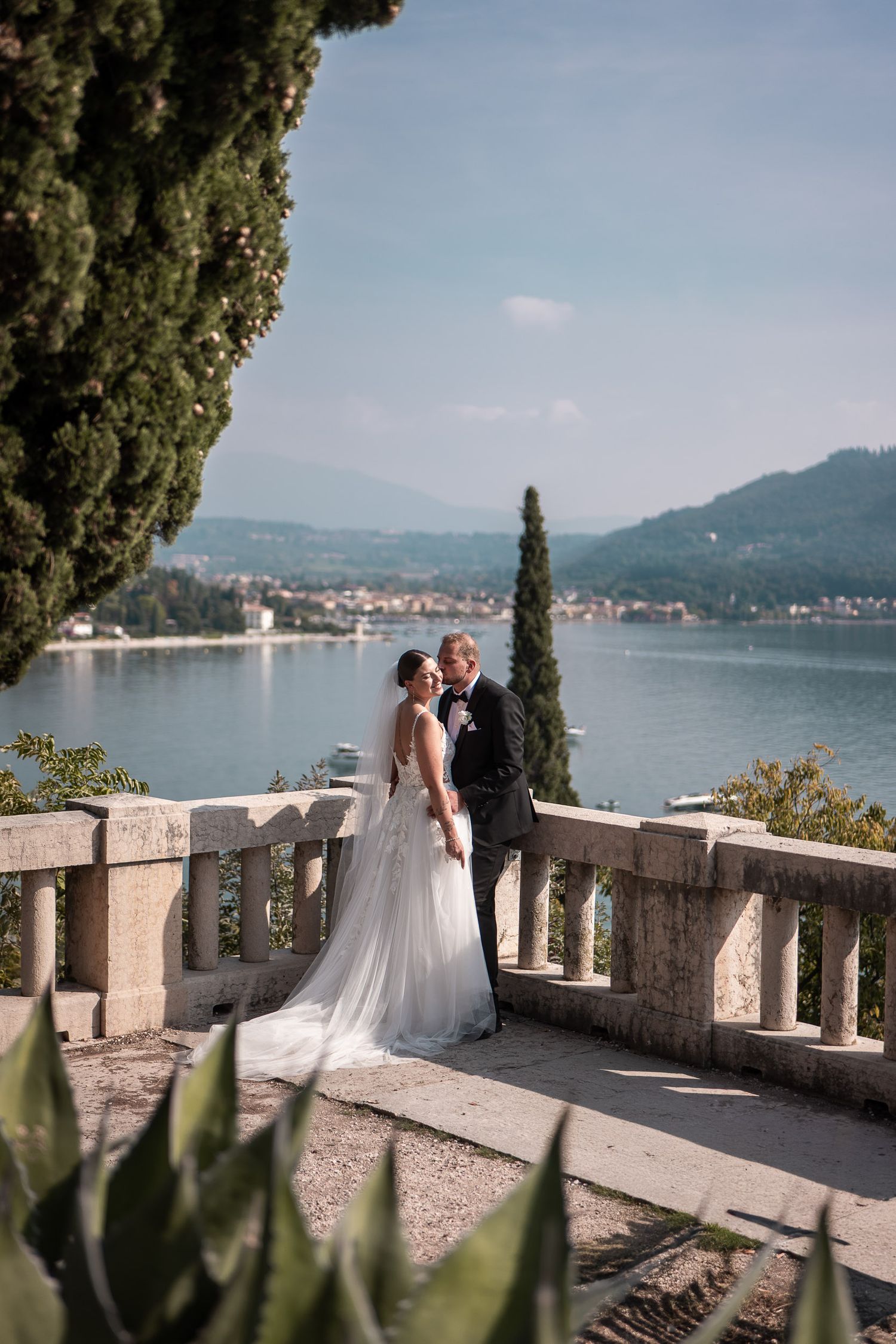 Brautpaar küsst sich auf einer Terrasse mit Panorama-Blick über den Gardasee in Bardolino.