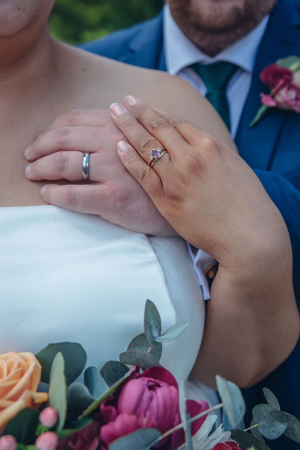Close-up of wedding rings and hands with colorful bouquet details.