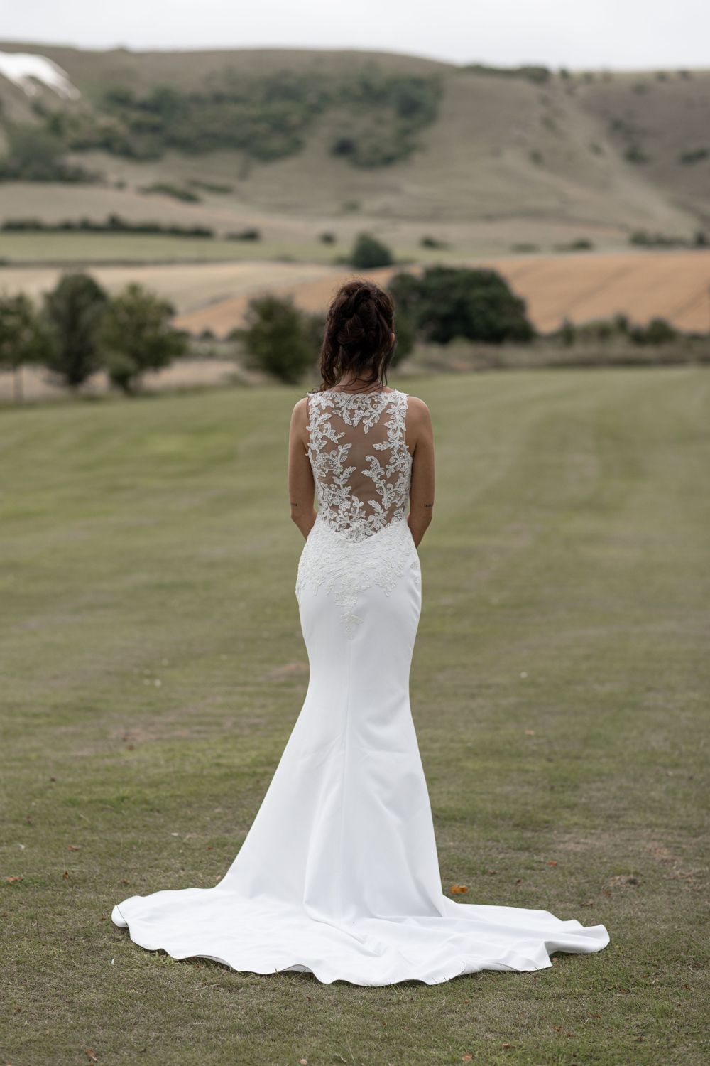 Elegant lace-back wedding dress showcased against rolling hills and countryside.