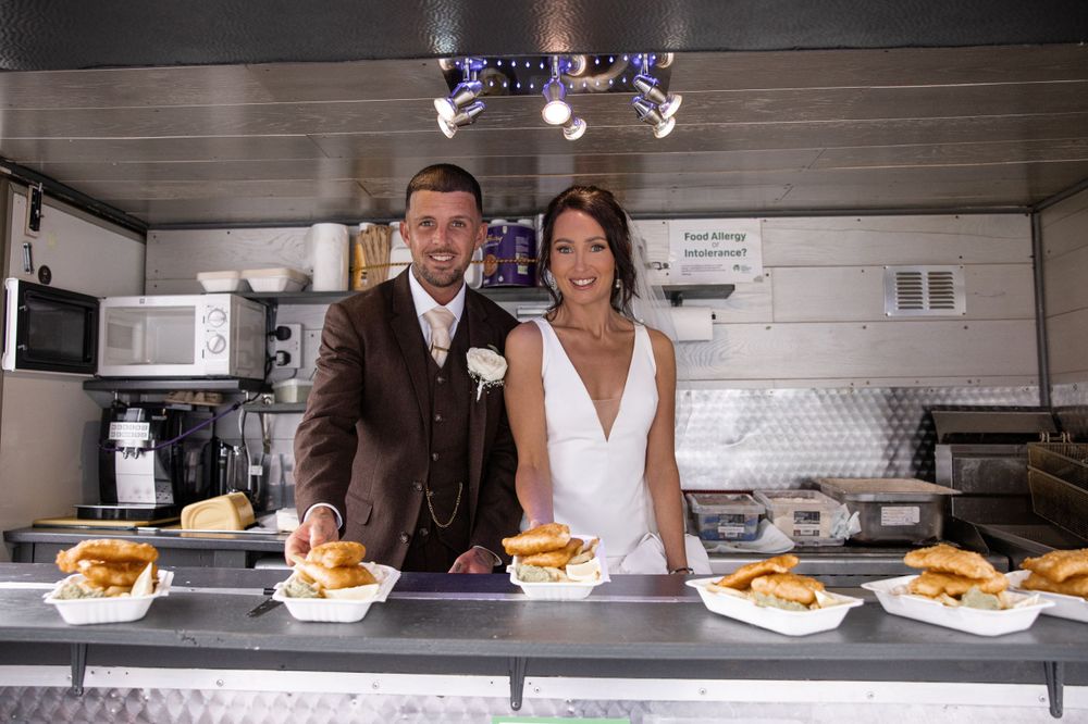 Newlyweds standing behind a food service counter with prepared plates.